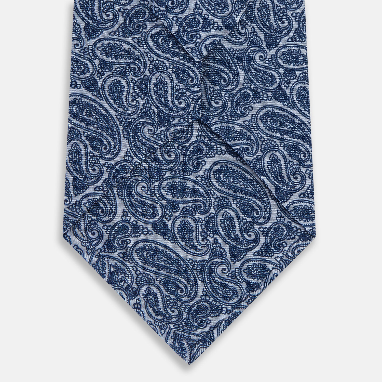 View 3 of product The Turnbull & Asser Pale Blue Paisley Printed Silk Tie is displayed rolled up on a white background, showcasing its intricate paisley pattern in varied blue tones.
