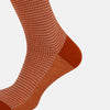 View 4 of product The Turnbull & Asser SOCKS LONG COTTON HOUNDSTOOTH ROSE is a single over-the-calf sock in rusty orange with a white houndstooth pattern and solid orange toe, heel, and cuff, shown on a plain white background.