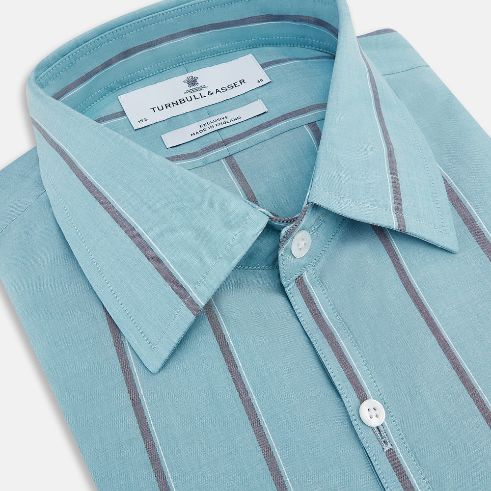 The Cendre Blue Track Stripe Westminster Shirt by Turnbull & Asser features a light blue hue, dark vertical stripes, button-down front, classic collar, and buttoned cuffs—showcasing British craftsmanship.