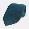 View 1 of product The Turnbull & Asser Turquoise Micro Hexagon Tie features refined British elegance with its small blue hexagonal pattern on a lighter background, neatly rolled and displayed on a plain white surface.