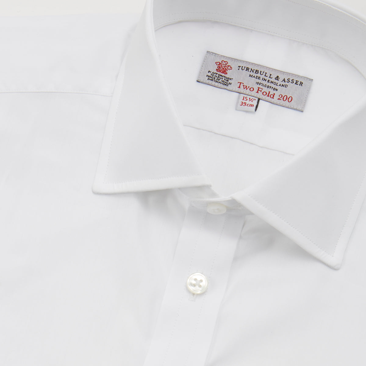 View 5 of product A neatly folded Turnbull & Asser Two-Fold 200 White Cotton Shirt with a Regent collar and 3-button cuffs, crafted from breathable fabric, is displayed on a light grey background with the label visible inside the collar.