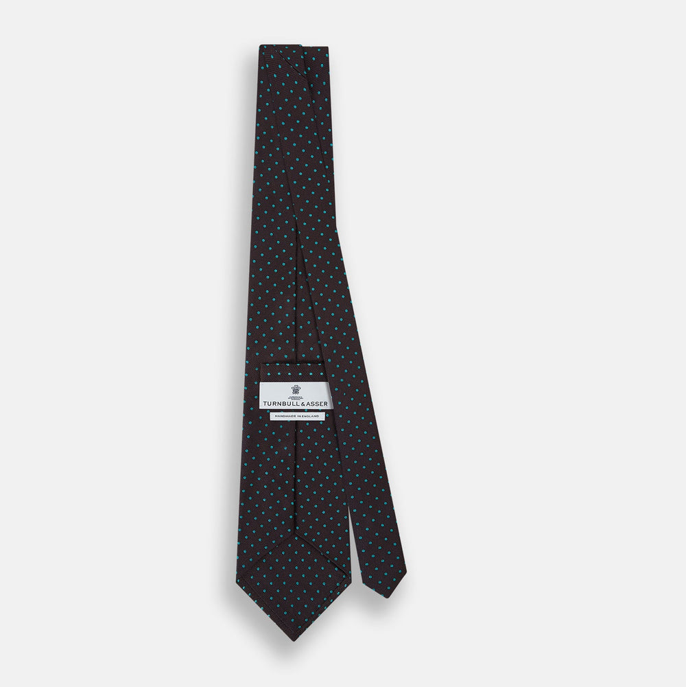 The Turnbull & Asser Turquoise and Forest Green Micro Dot Silk Tie is rolled up, showcasing evenly spaced micro dots on silk, displayed against a plain white background.