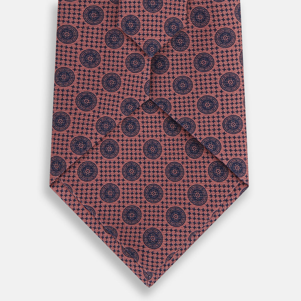 The Turnbull & Asser Antique Pink Medallion Silk Tie features a rolled-up design with small dark blue circular motifs on a white background.