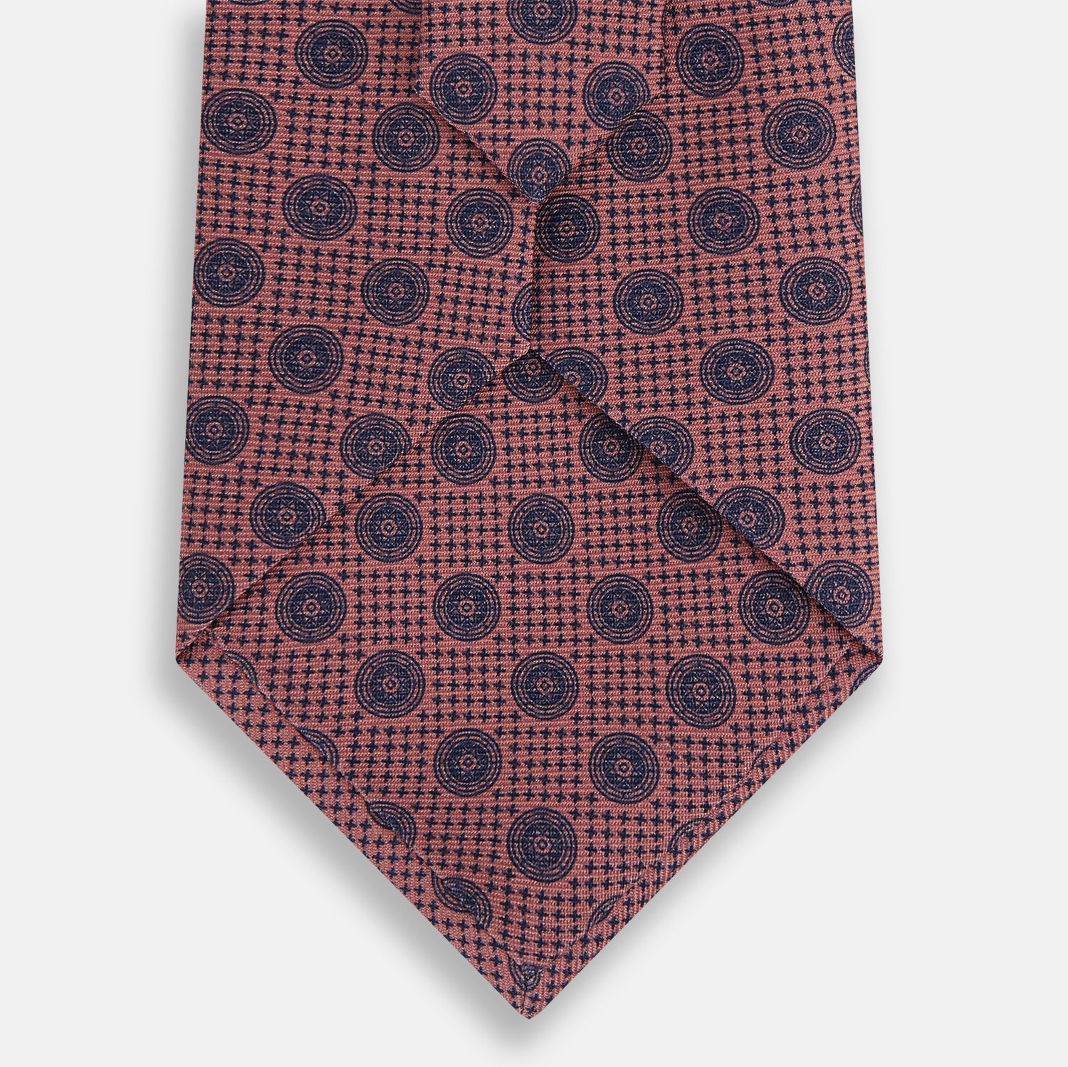 View 3 of product The Turnbull & Asser Antique Pink Medallion Silk Tie features a rolled-up design with small dark blue circular motifs on a white background.