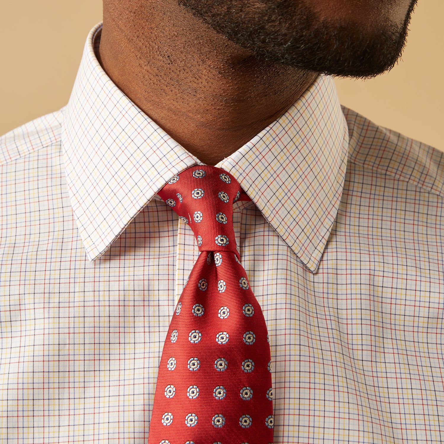 View 4 of product A man stands against a beige background, facing forward with a neutral expression and arms relaxed, wearing the Turnbull & Asser Red Multi Check Regular Fit Mayfair Shirt.