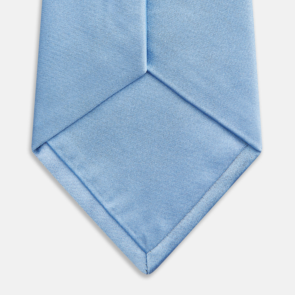 The Turnbull & Asser SATIN RIVER TIE, a neatly rolled light blue silk accessory with a smooth matte finish, is displayed against a plain white background.