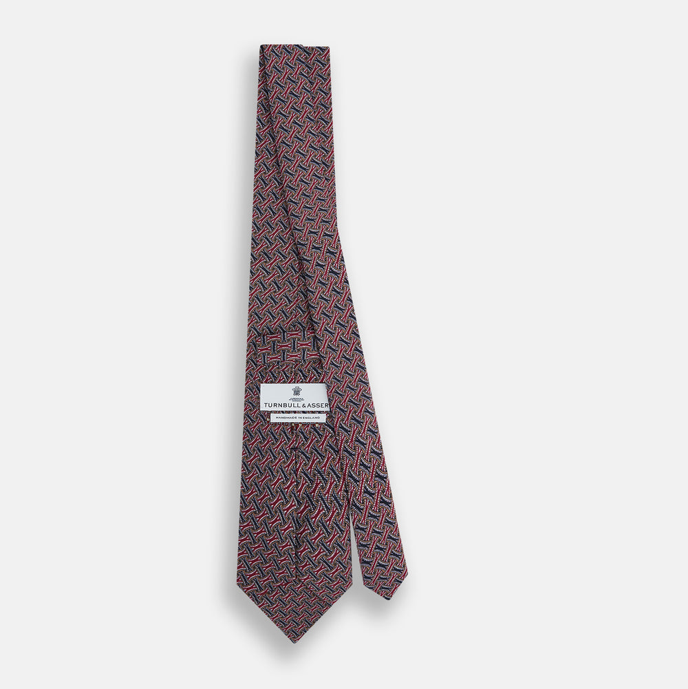 The Turnbull & Asser Burgundy and Navy Weave-Patterned Printed Silk Tie features an intricate geometric design, shown rolled on a plain white background.