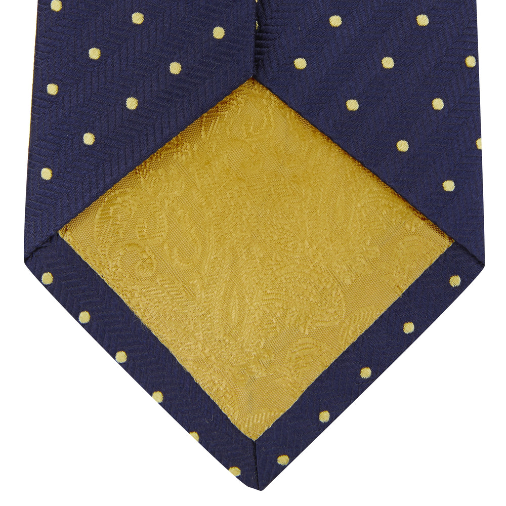 The Turnbull & Asser Navy Spot Woven Herringbone Silk Tie features a navy blue base with evenly spaced yellow polka dots, making it an essential accessory for smart attire. Displayed rolled on a white background.