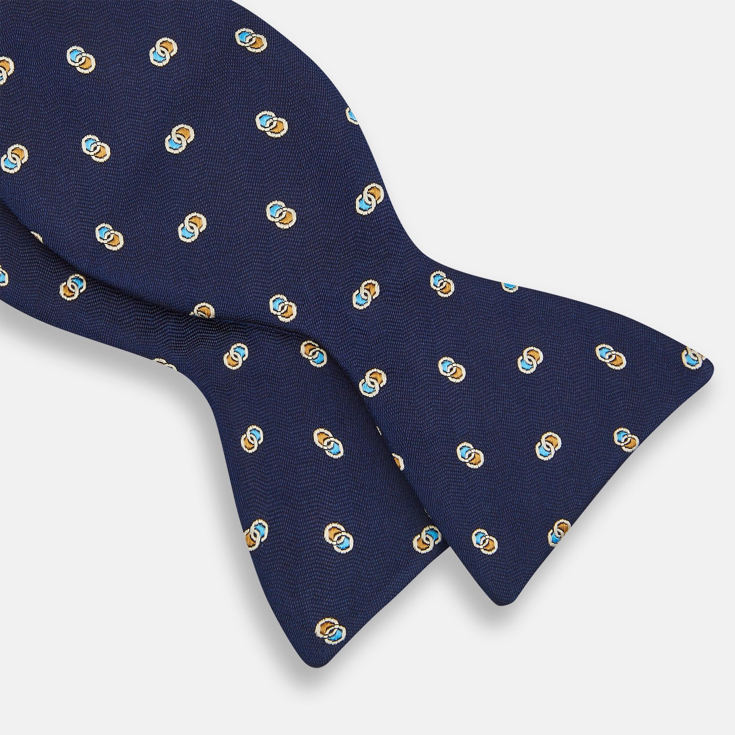 View 3 of product The Blue and Yellow Links Silk Bow Tie by Turnbull & Asser features a subtle wavy texture with a refined pattern of interlinked gold, blue, and white rings—an elegant accessory to enhance any formal outfit.