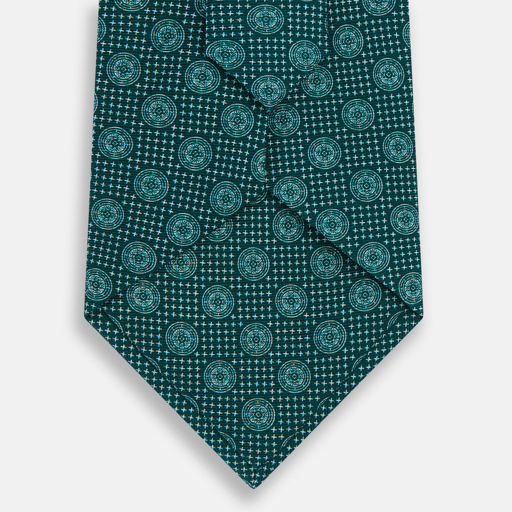The Forest Green Medallion Printed Silk Tie by Turnbull & Asser features a repeating medallion pattern in lighter green tones, crafted from English silk and shown rolled up on a plain white background.