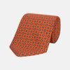 View 1 of product The Great Gatsby Orange Printed Silk Tie by Turnbull & Asser, from the Legends collection, features a repeating pattern of small blue, white, and yellow floral motifs—an ideal summer accessory—shown rolled on a white background.