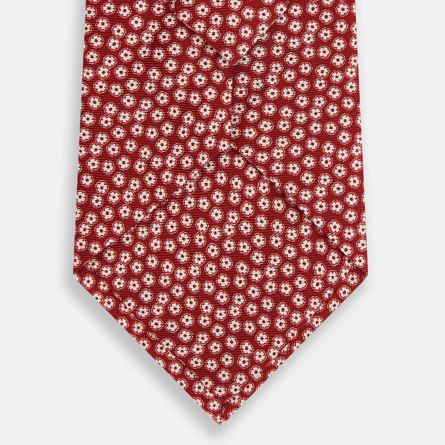 View 3 of product The Turnbull & Asser Red Flower-Patterned Printed Silk Tie, made from fine English silk, features a repeating white floral design and is shown rolled on a plain white background.
