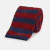 View 1 of product The Turnbull & Asser KNITTED STRIPE RED TIE features bold red and navy wide stripes in a rolled-up, knitted design—an eye-catching accessory shown on a plain white background.