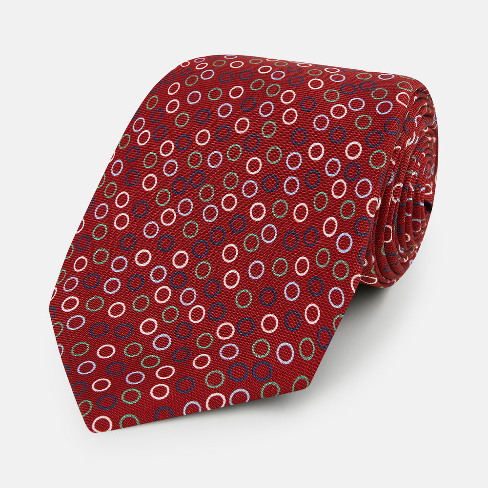 The Pink and Navy Circle Red Printed Silk Tie by Turnbull & Asser showcases English silk craftsmanship with a pattern of multicolored circles on rich red silk, elegantly displayed against a plain white background.