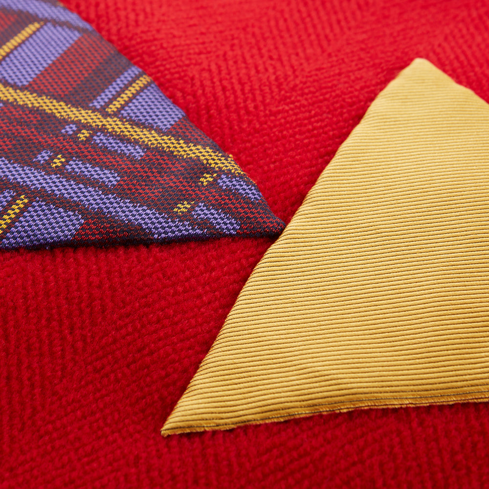 The Turnbull & Asser Red Applique Hand Stitched Lambswool Blanket features black-stitched edges and handsewn tie silk patches, including a yellow triangle and plaid triangle arranged to form a stylized fish.