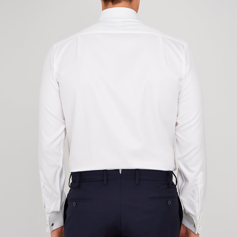 A neatly folded Turnbull & Asser White Oxford Shirt with T&A collar and double cuffs is displayed on a light blue background.