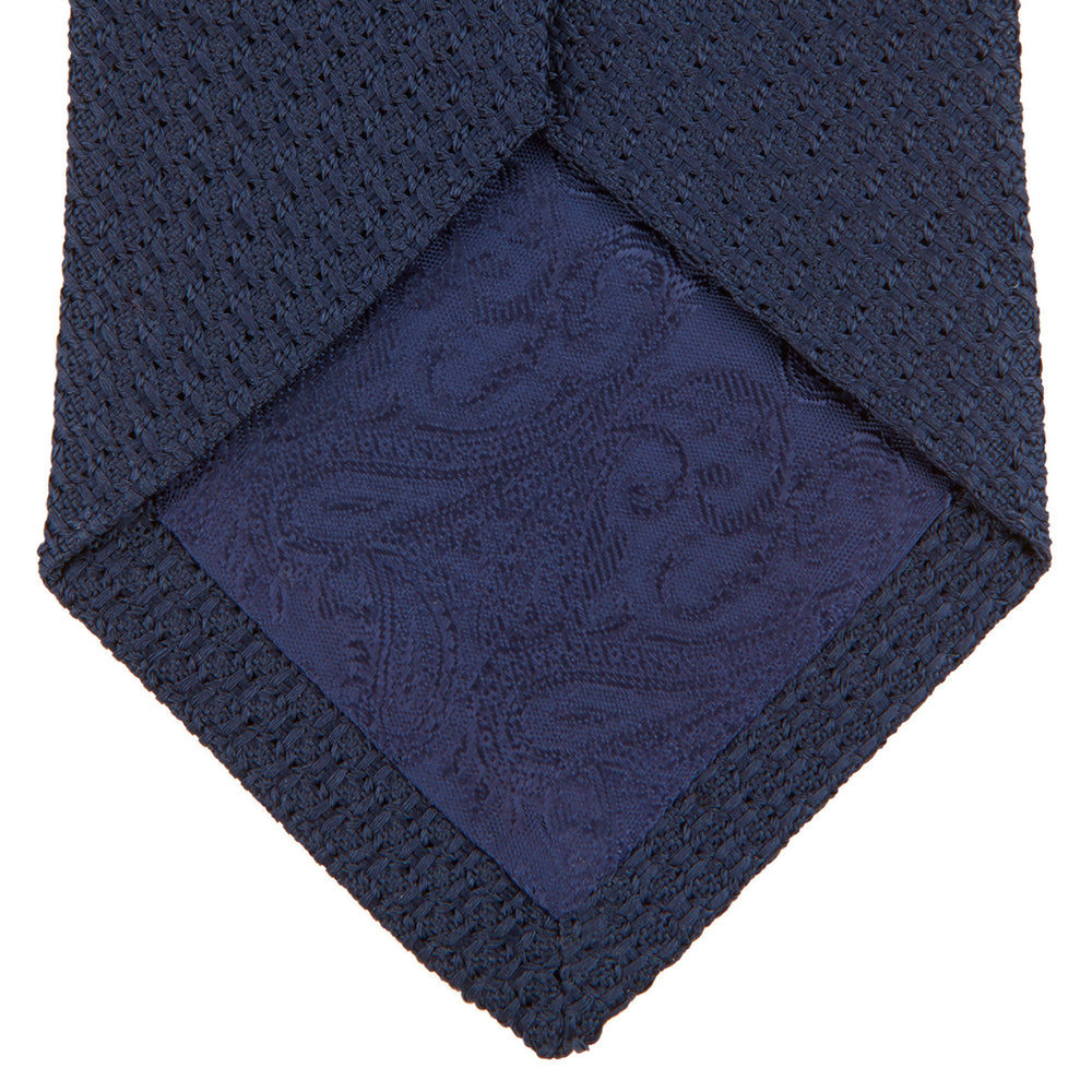 The Turnbull & Asser Navy Plain Woven Grenadine Silk Tie, an essential accessory, is rolled at one end and displayed on a plain white background.