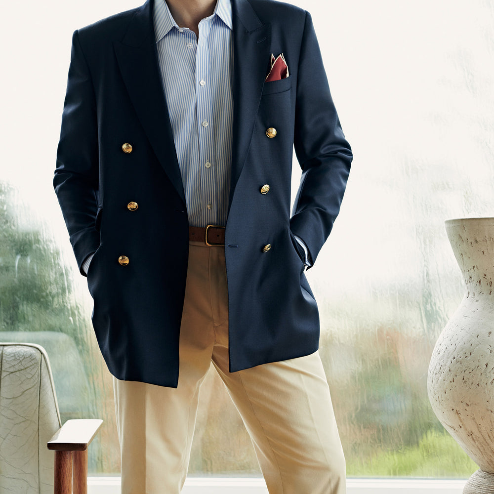 The Classic Navy Wool Blazer by Turnbull & Asser is a nautical double-breasted jacket with gold buttons, peaked lapels, three front pockets on one side, one on the other, and four gold buttons per cuff, shown against a white background.