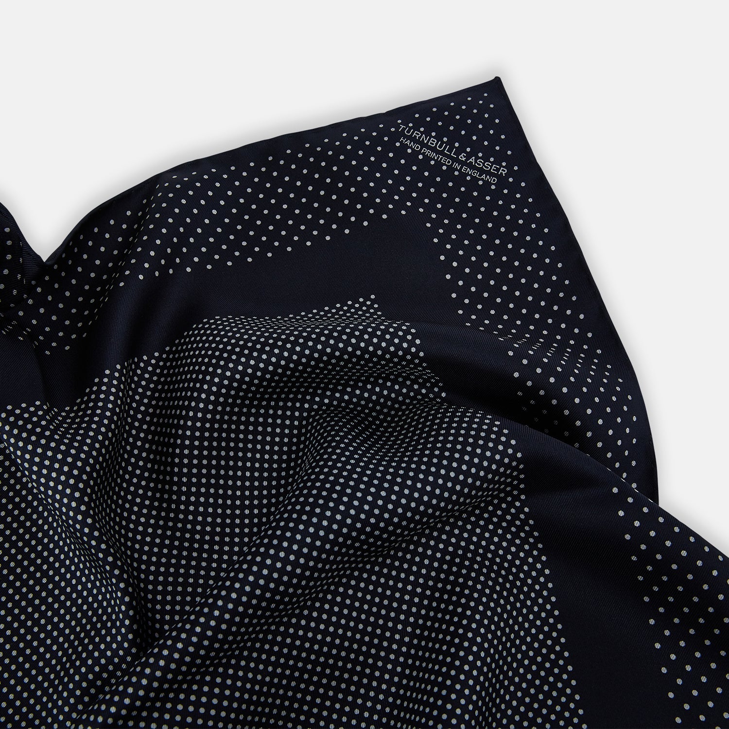 View 2 of product The Turnbull & Asser Navy and Grey Dot Silk Pocket Square features a neatly folded design with small grey dots on navy silk and a solid border, showcasing both sides of the luxurious fabric.
