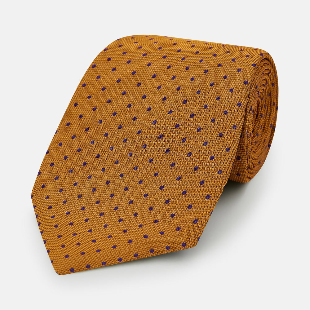 The Turnbull & Asser Purple and Orange Micro Dot Silk Tie features a pattern of small blue dots, shown rolled up on a white background.