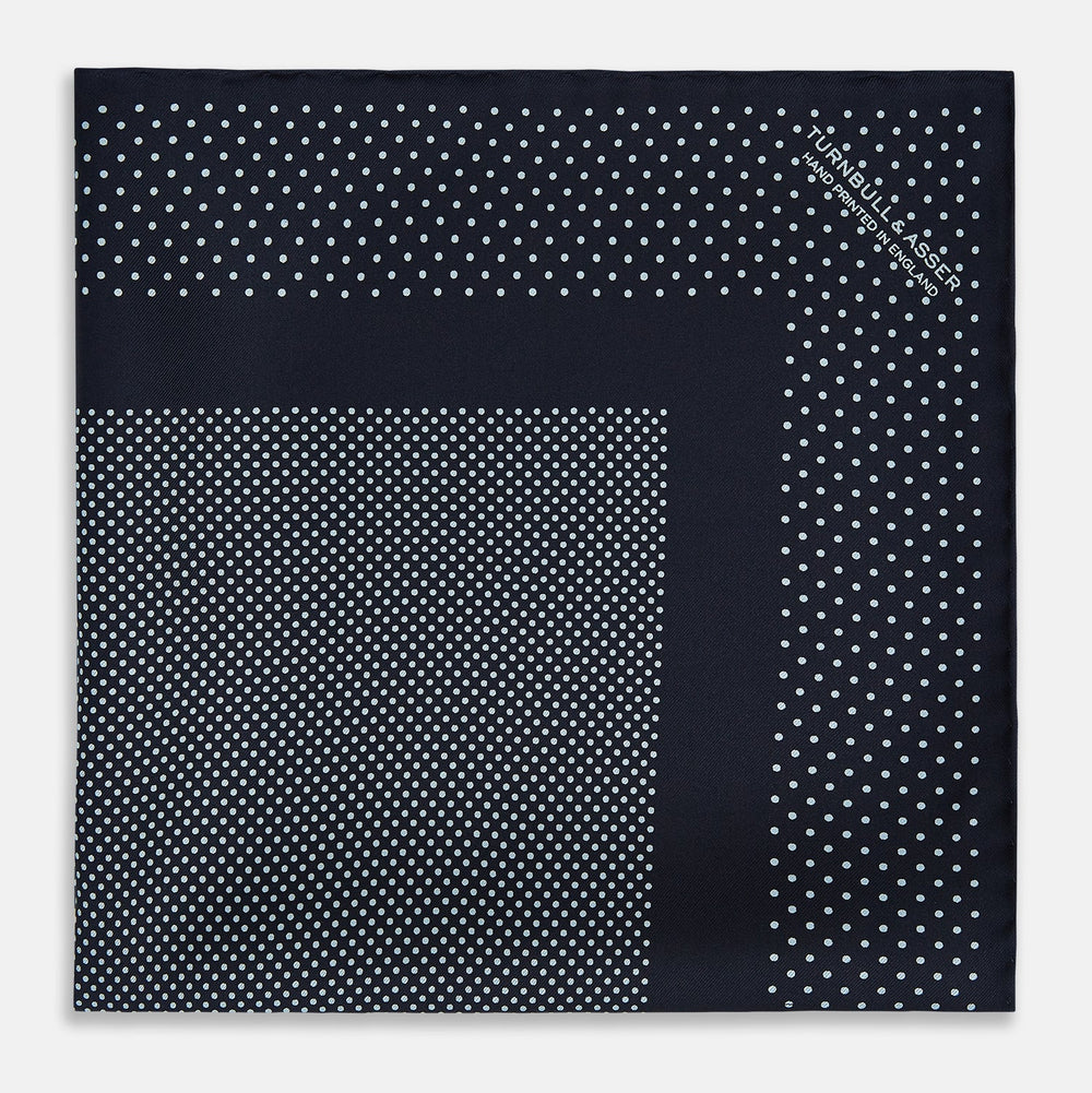 The Turnbull & Asser Navy and Light Blue Dot Silk Pocket Square features white polka dots, a contrasting border, and an inner square design, showcasing handmade craftsmanship with its expertly folded finish.