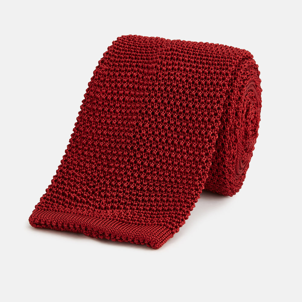 The Turnbull & Asser KNITTED RED SILK PLAIN TIE, featuring a textured finish, is rolled up and displayed against a plain white background.