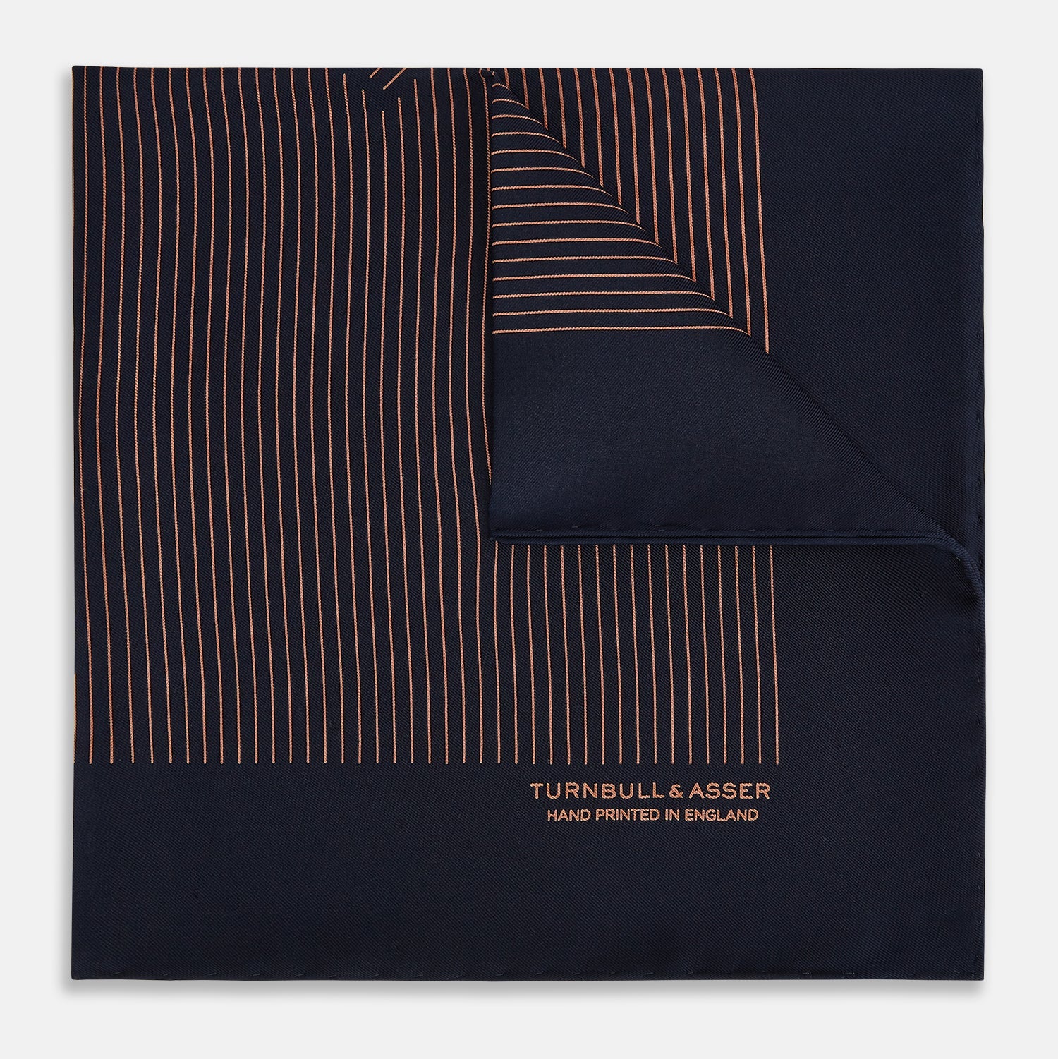 View 1 of product The Turnbull & Asser Navy and Blush Stripe Silk Pocket Square features thin blush stripes on navy silk, finished with "TURNBULL & ASSER HAND PRINTED IN ENGLAND" in the corner, highlighting its refined English craftsmanship.
