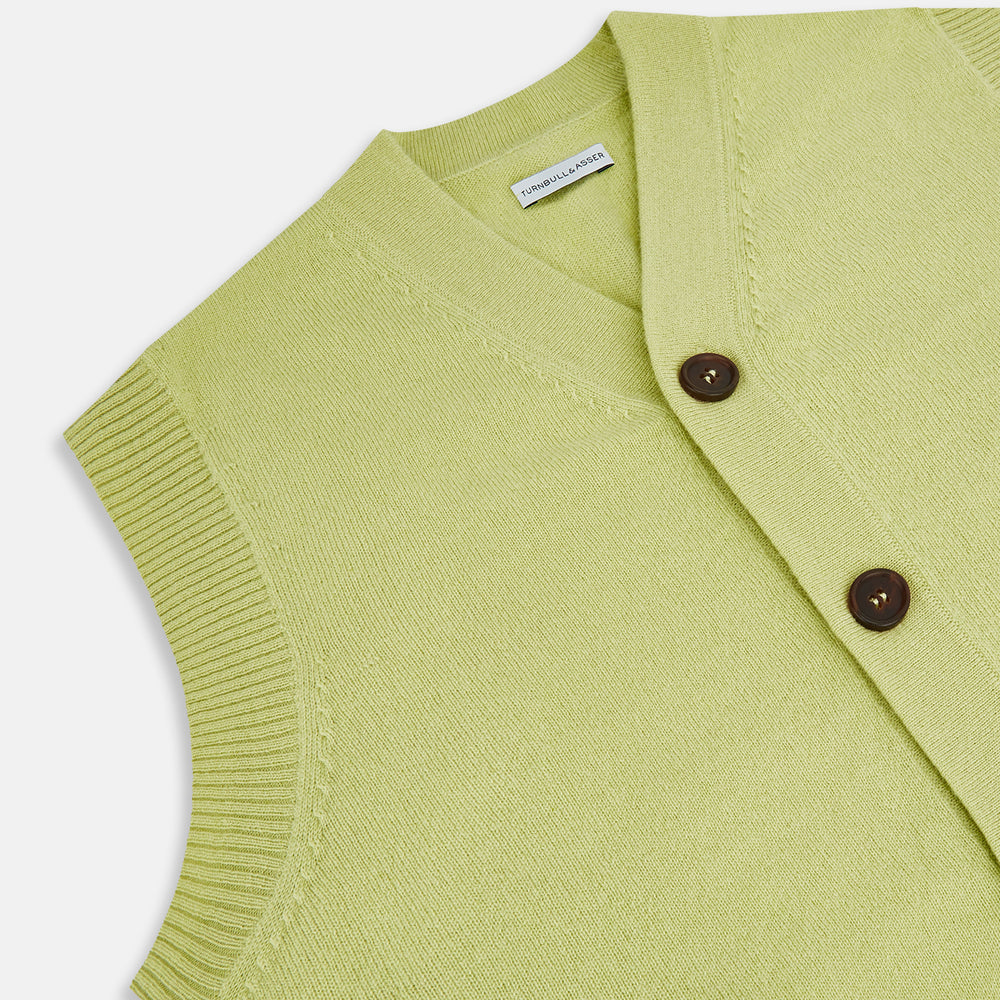 The Melon Green Sleeveless Cardigan by Turnbull & Asser features a ribbed collar, large brown buttons, and two front pockets—a stylish layering piece shown against a plain white background.