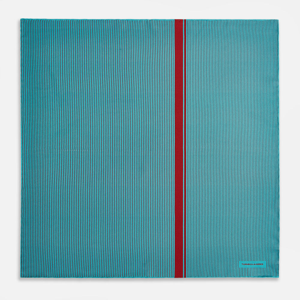 The Turnbull & Asser Turquoise and Red Stripe Silk Pocket Square features thin navy stripes with a bold vertical red stripe, partially folded to reveal the reverse pattern and the brand's logo, showcasing its British heritage.