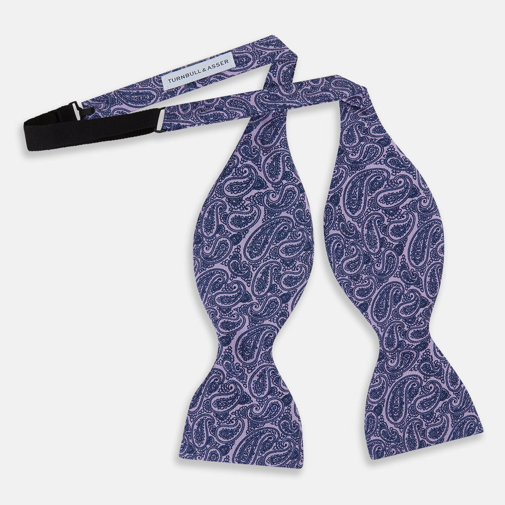 The Turnbull & Asser Lilac Paisley Silk Bow Tie features a refined dark blue pattern on lilac silk, shown on a plain white background—an elegant men's accessory for any occasion.