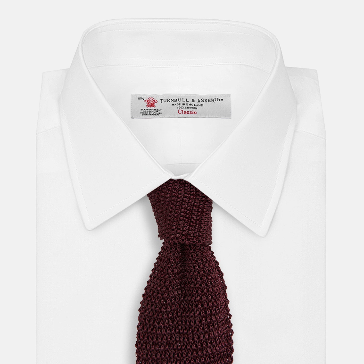 View 2 of product The Turnbull & Asser Knitted Burgundy Square Silk Plain Tie, featuring a textured open-weave pattern, is rolled up and displayed on a plain white background—a versatile accessory for the modern gentleman.