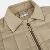 View 2 of product The Battersea Sand Quilted Jacket by Turnbull & Asser is a light beige men's jacket with a front zipper, pointed collar, zippered side pockets, chest pocket, and buttoned cuffs, shown on a plain white background.