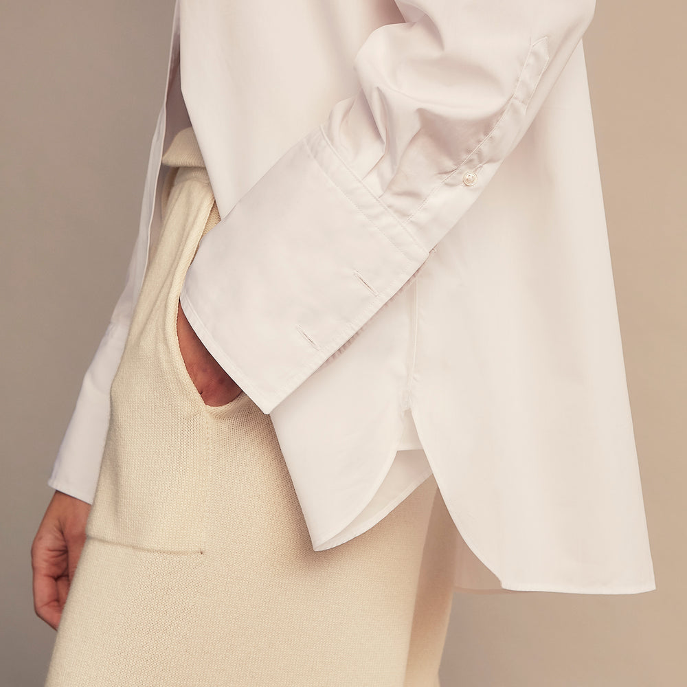 A woman with straight brown hair pulled back wears the Turnbull & Asser White Cotton Marlene Shirt, featuring classic menswear details, paired with high-waisted cream trousers against a neutral background.