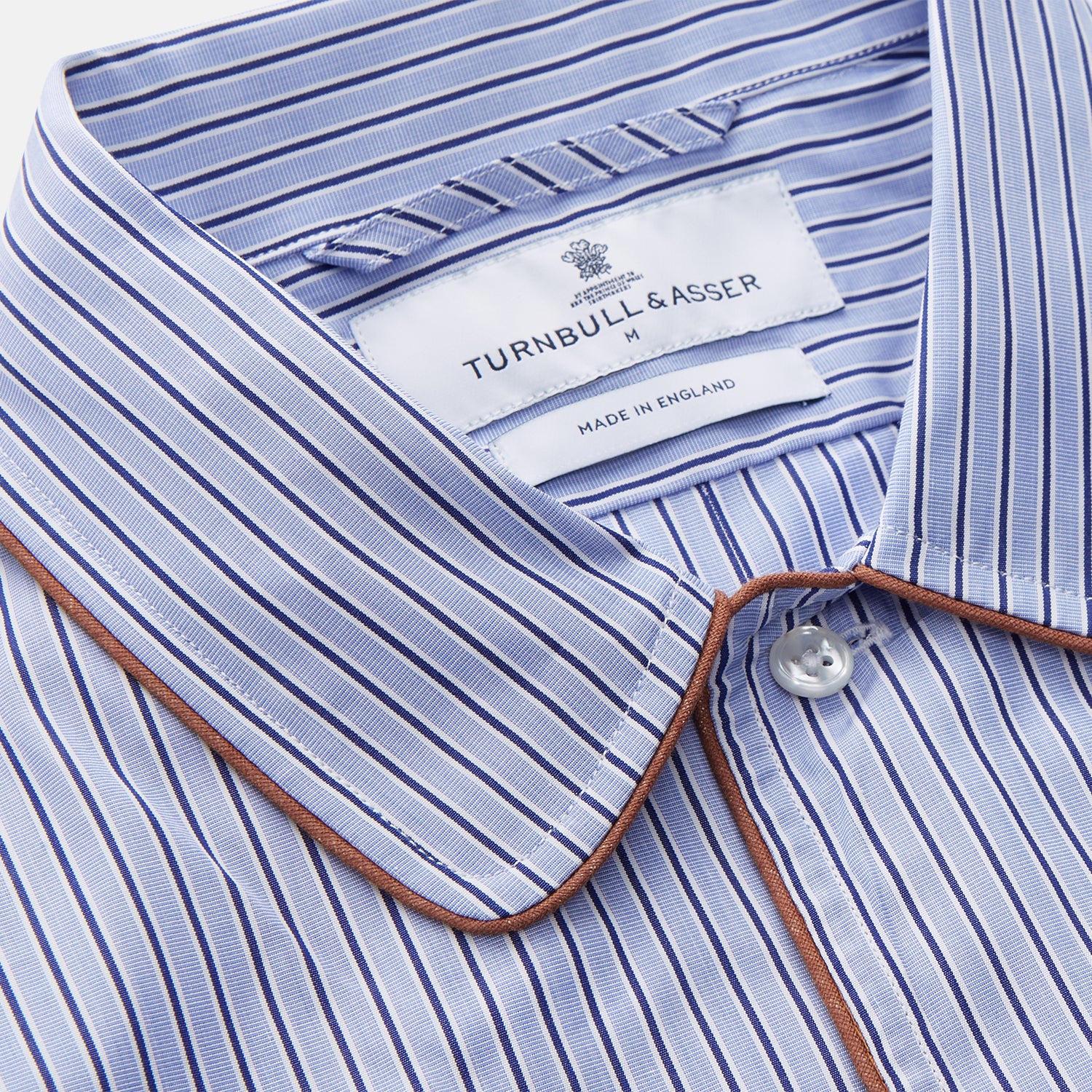 View 4 of product The Blue and Navy Halo Stripe Cotton Sussex Nightshirt by Turnbull & Asser features long sleeves, a collar, button-down front, chest pocket, curved hem, and brown piping for a classic luxury sleepwear style.