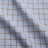 View 4 of product A man wearing glasses and a Pale Blue Multi Check Cashmerello Holiday Fit Winnington Shirt by Turnbull & Asser leans casually against a white countertop, looking at the camera with a neutral expression.