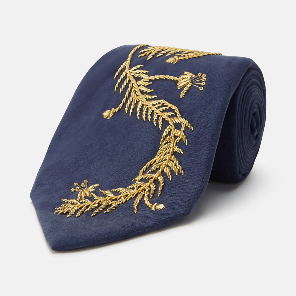 The Turnbull & Asser Navy Gold Embroidered Botanical Tie features intricate gold botanical embroidery on navy blue silk, neatly rolled with the detailed tip facing forward.