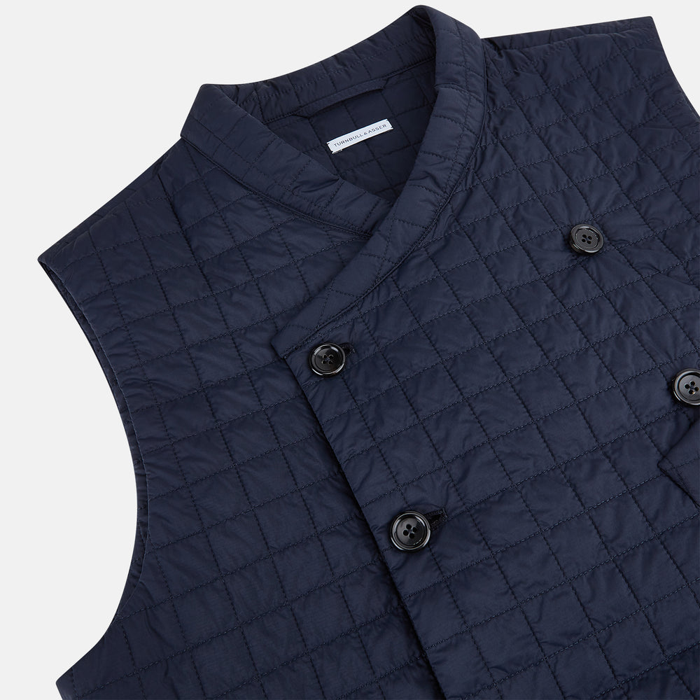 The Turnbull & Asser Navy Double-Breasted Quilted Gilet is a sleeveless piece with an asymmetrical button closure, chest pocket, and two zippered side pockets, shown on a plain white background—ideal for layered dressing.