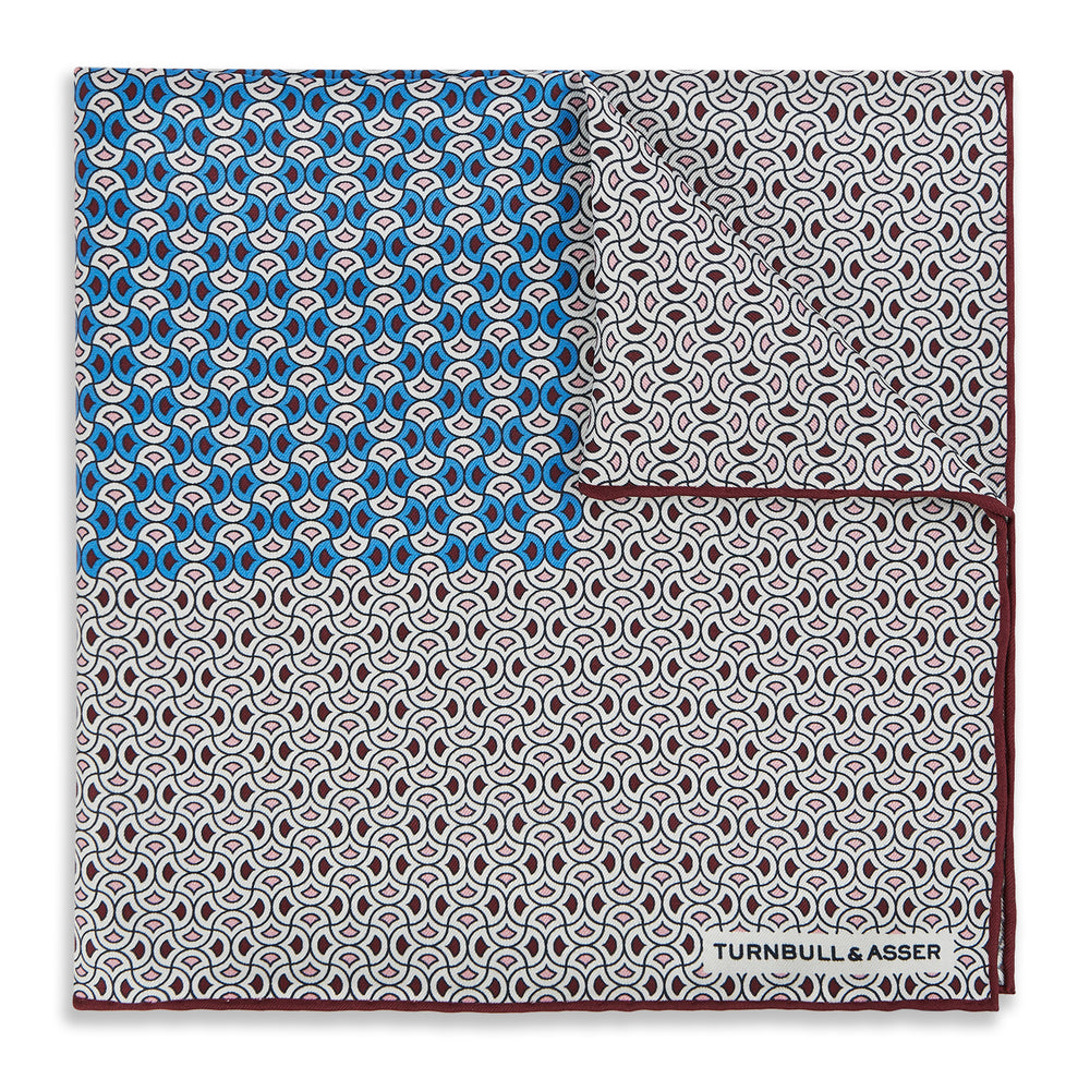 A geometric brown and blue silk pocket square from Turnbull & Asser UK, predominantly white with maroon and blue accents that suggest subtle burgundy tones, featuring a bold blue section in the top left corner and elegantly finished with the TURNBULL & ASSER branding in one corner.