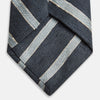 View 4 of product The Turnbull & Asser Blue & Silver Stripe Silk Tie, featuring wide diagonal stripes, is rolled up and displayed against a plain white background.