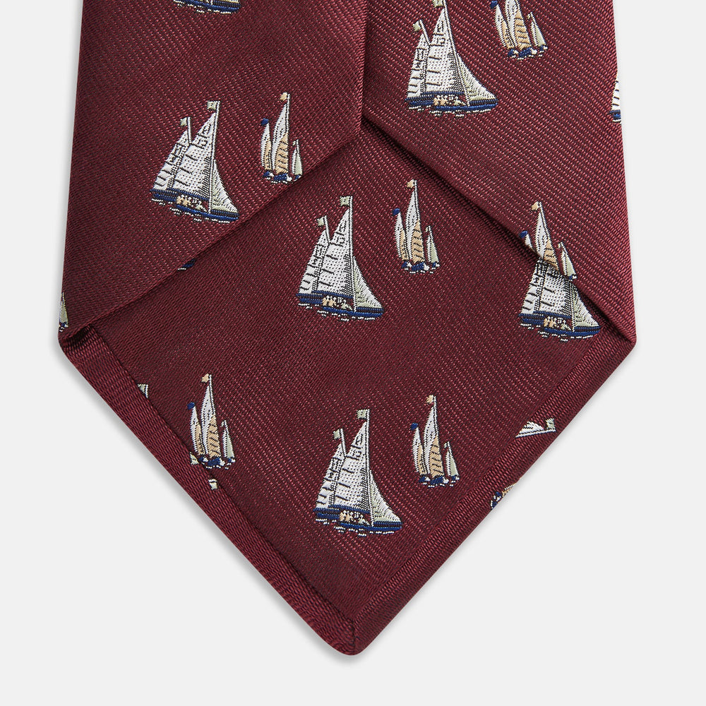 The Turnbull & Asser Burgundy Racing Yachts Silk Tie features a nautical sailboat pattern in white, blue, and brown on burgundy silk, shown rolled up against a plain white background.