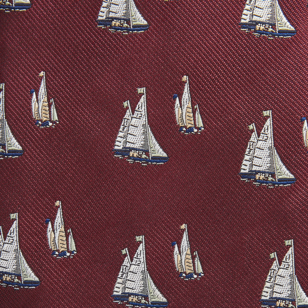 The Turnbull & Asser Burgundy Racing Yachts Silk Tie features a nautical sailboat pattern in white, blue, and brown on burgundy silk, shown rolled up against a plain white background.