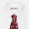 View 4 of product The Turnbull & Asser Burgundy Racing Yachts Silk Tie features a nautical sailboat pattern in white, blue, and brown on burgundy silk, shown rolled up against a plain white background.
