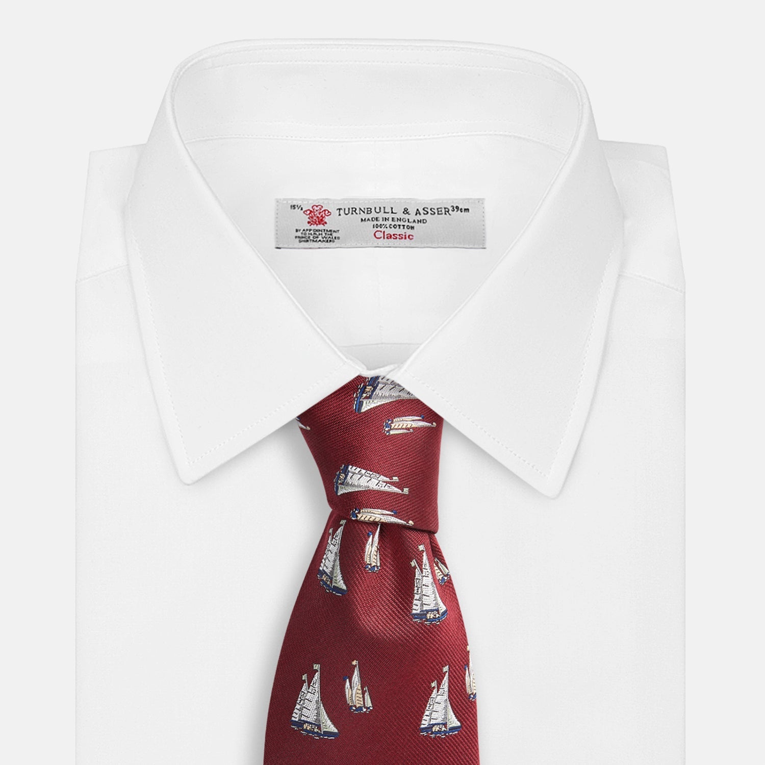 View 4 of product The Turnbull & Asser Burgundy Racing Yachts Silk Tie features a nautical sailboat pattern in white, blue, and brown on burgundy silk, shown rolled up against a plain white background.