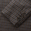 View 4 of product A man in glasses and a Turnbull & Asser Brown & Blue Check Merino Barrington Blazer, detailed with a colorful pocket square, stands thoughtfully indoors by patterned curtains, gazing out the window.
