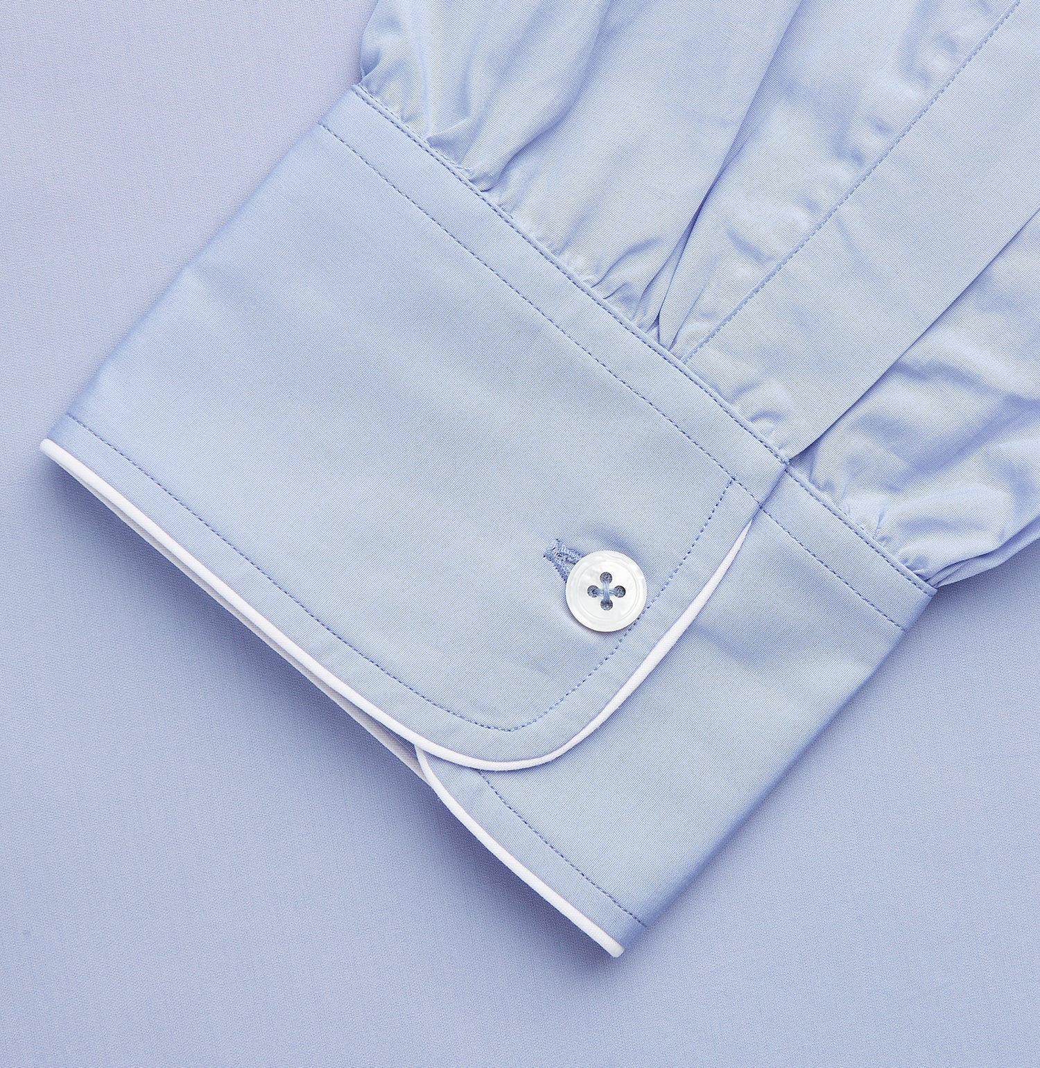 View 4 of product The Turnbull & Asser Blue Piped Sea Island Quality Cotton Nightshirt features light blue sea island cotton, a collared neckline with white piping, a front pocket, partial button placket, and a curved high-low hem for classic nightshirt style.
