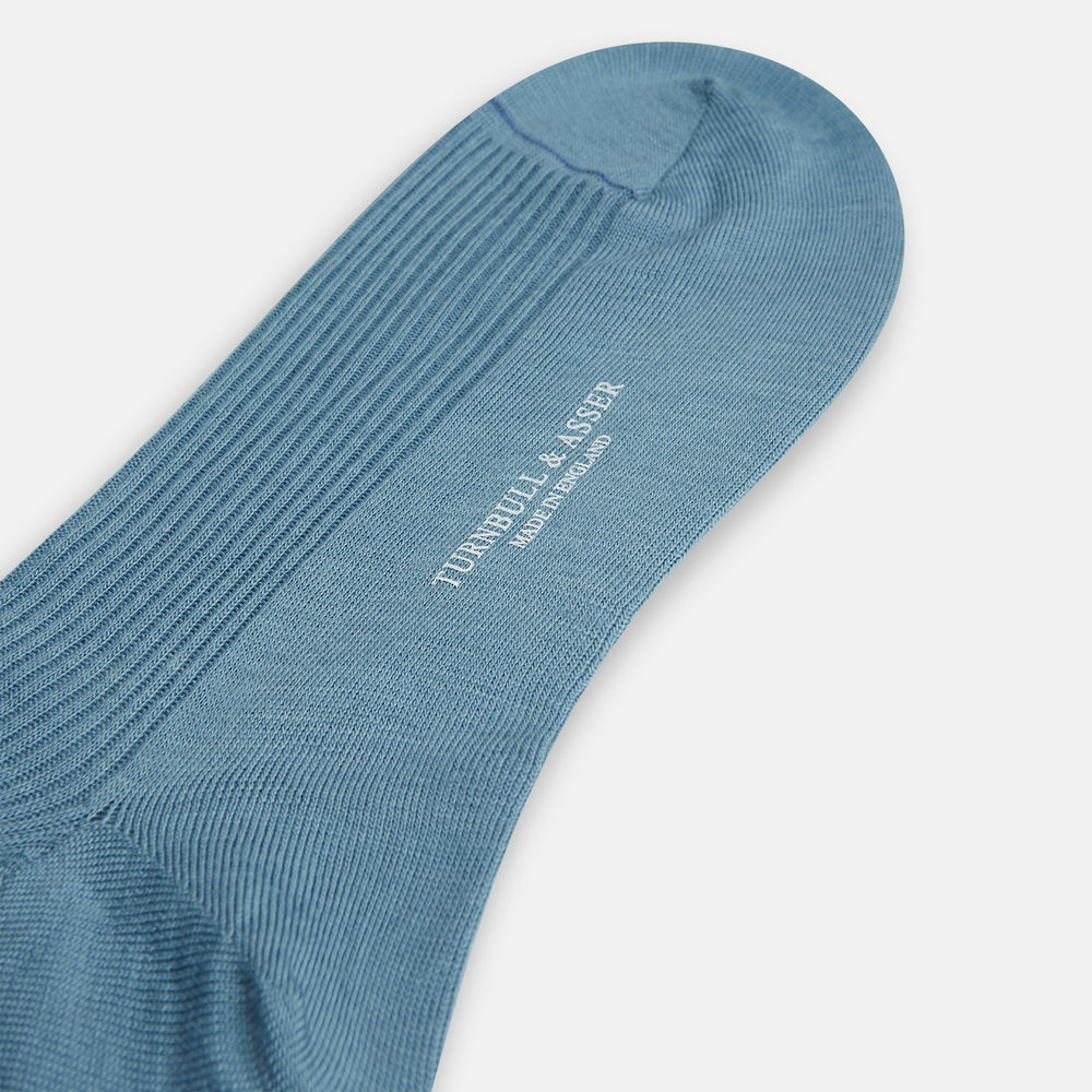A single Pale Blue Mid-Length Merino Sock by Turnbull & Asser stands upright against a white background, highlighting its ribbed texture and reinforced toe and heel—showcasing the elegance of luxury merino wool.