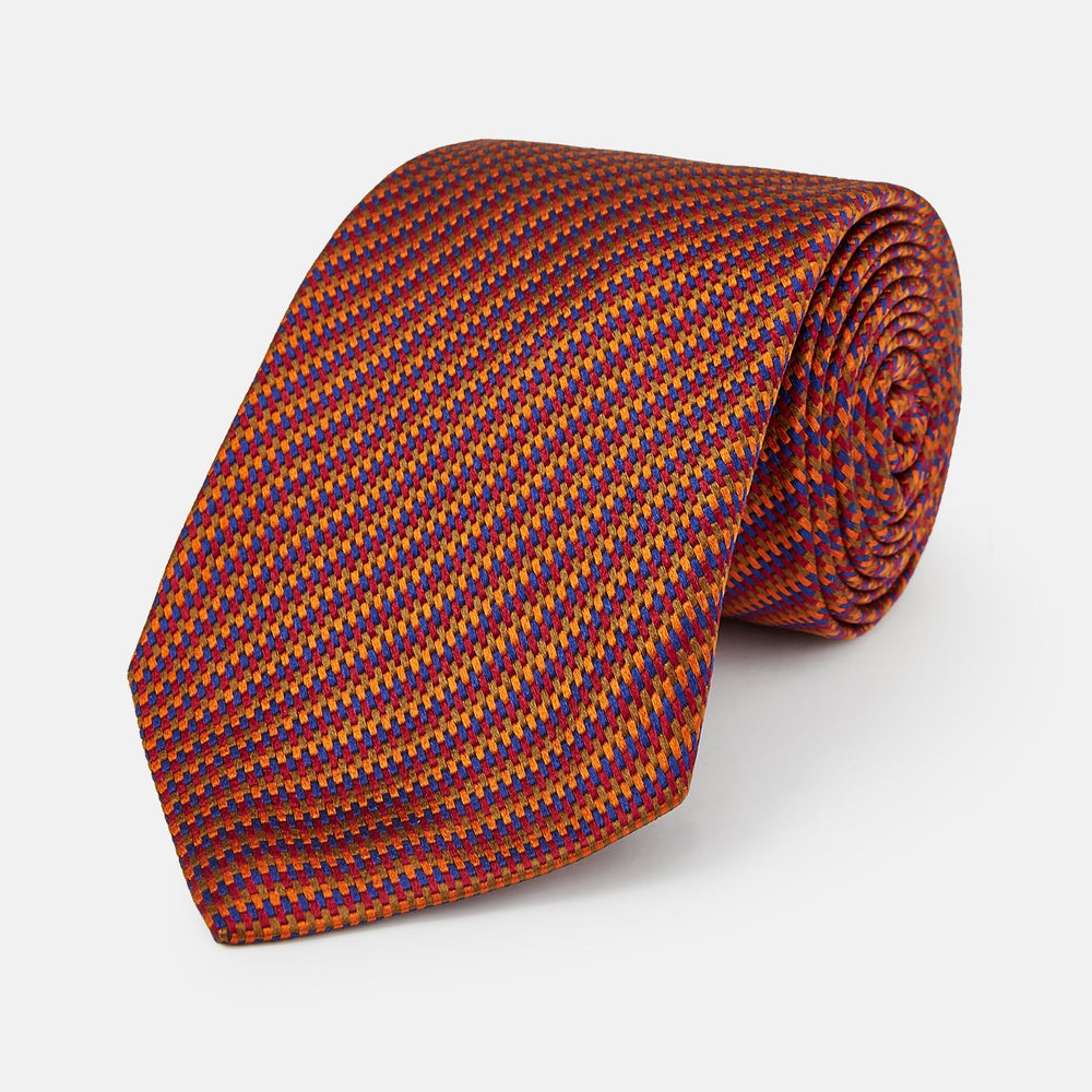 The Turnbull & Asser Die Another Day Stripe Silk Tie, as seen on James Bond, showcases a vibrant orange, red, and purple woven pattern, elegantly rolled and displayed against a white background.