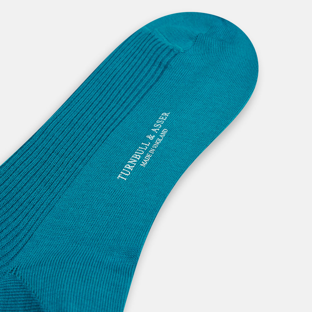 A Turnbull & Asser Turquoise Mid-Length Merino Sock stands upright on a plain light gray background, showcasing its ribbed texture and seamless toe.