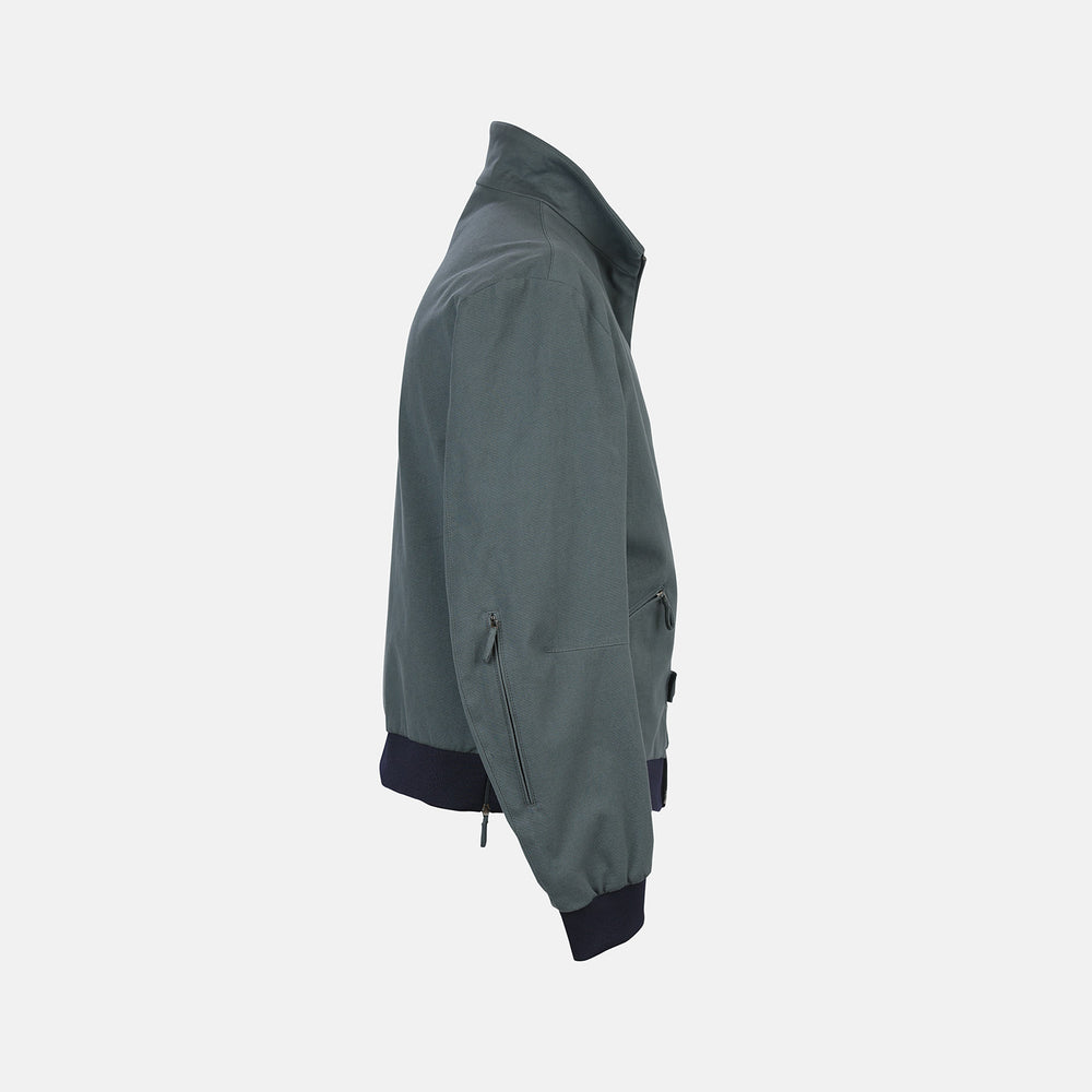 The Fairway Ash Grey Driving Jacket in Cotton by Turnbull & Asser UK features a zip-up design with a raised collar, black ribbed cuffs and hem, and multiple zippered pockets. Photographed on a plain white background, this essential piece from the Driver’s Capsule Collection is an iconic addition to any motoring wardrobe.
