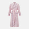 View 1 of product The Pink Check Cotton Gown by Turnbull & Asser UK is a long cotton dressing gown in a pink check pattern, featuring a belted waist, notched collar, long sleeves, and blue trim along the edges and pocket—perfect for relaxing in style.
